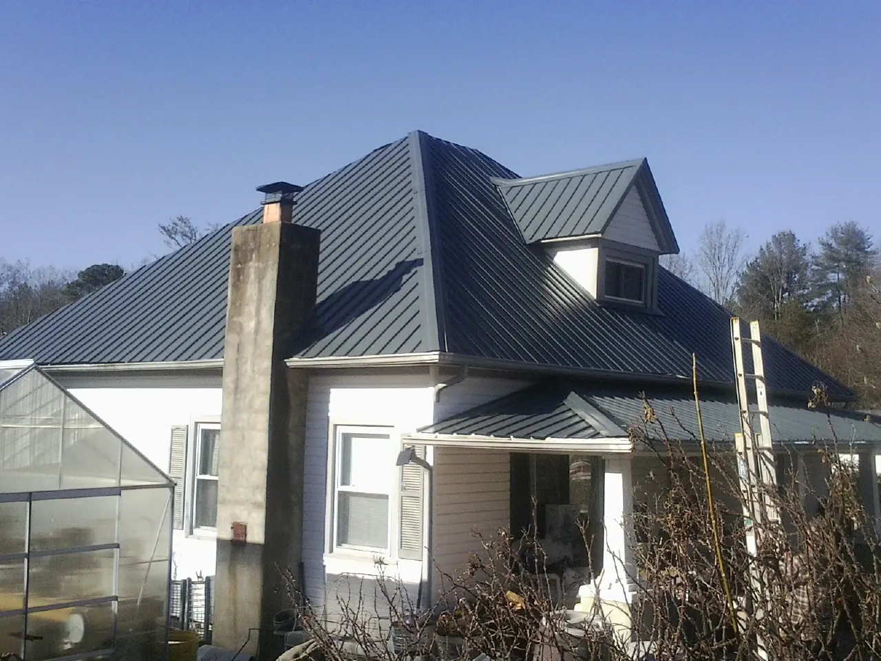 Dark blue standing seam metal roof on a white farmhouse with dormer — Slate & Tile Roof Repair by Roofing Brothers in Cinebar