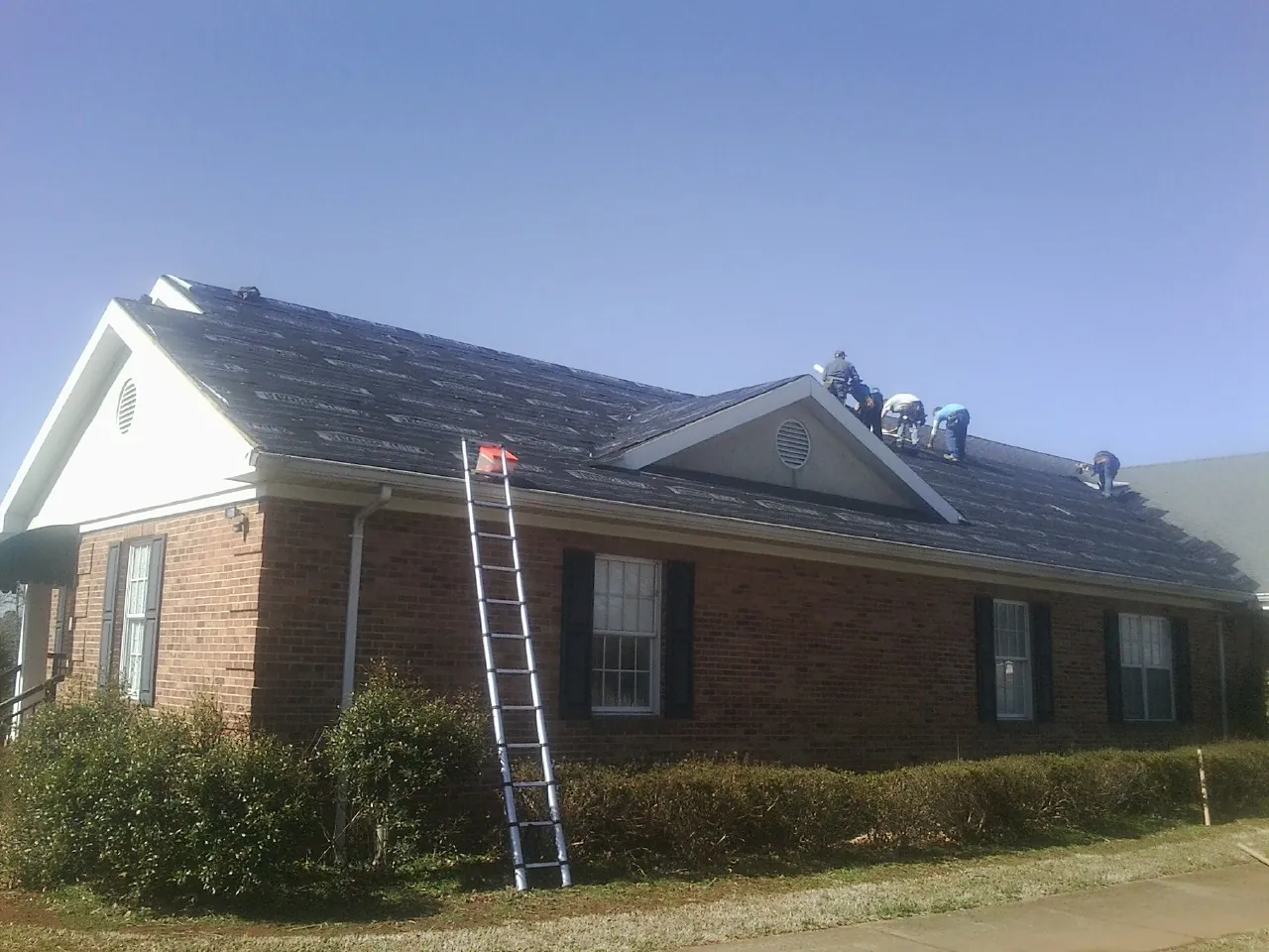 Crew tearing shingles off a brick ranch roof with a ladder set — Emergency Roof Repair work by our crew in Cinebar