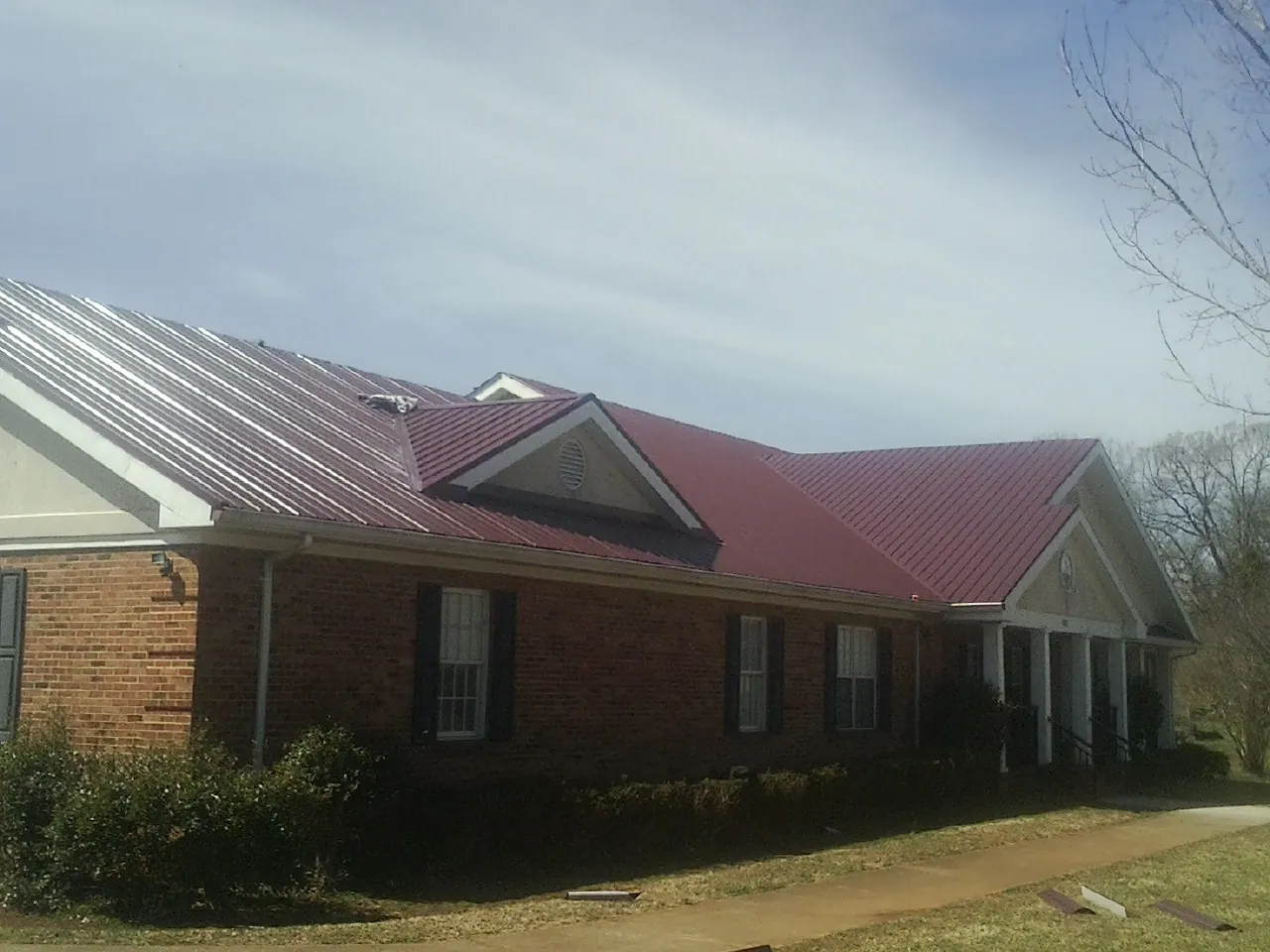 Red metal roof with gabled entries on a long brick building, from a Hail Damage Roof Repair job in Cinebar