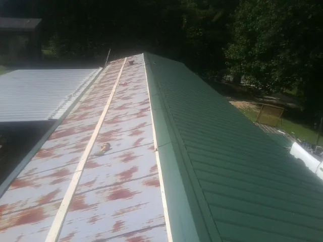 Old rusted panels beside newly installed green metal roofing — Wind Damage Roof Repair by Roofing Brothers in Cinebar