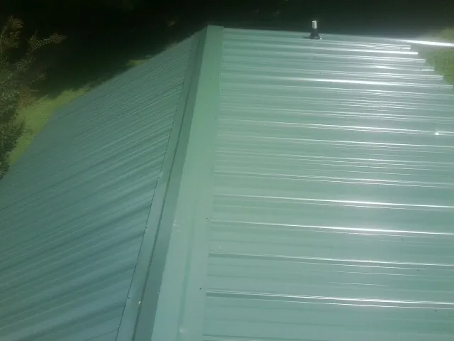 New green metal panels meeting at the ridge of a roof — Flat Roof Repair work by our crew in Cinebar