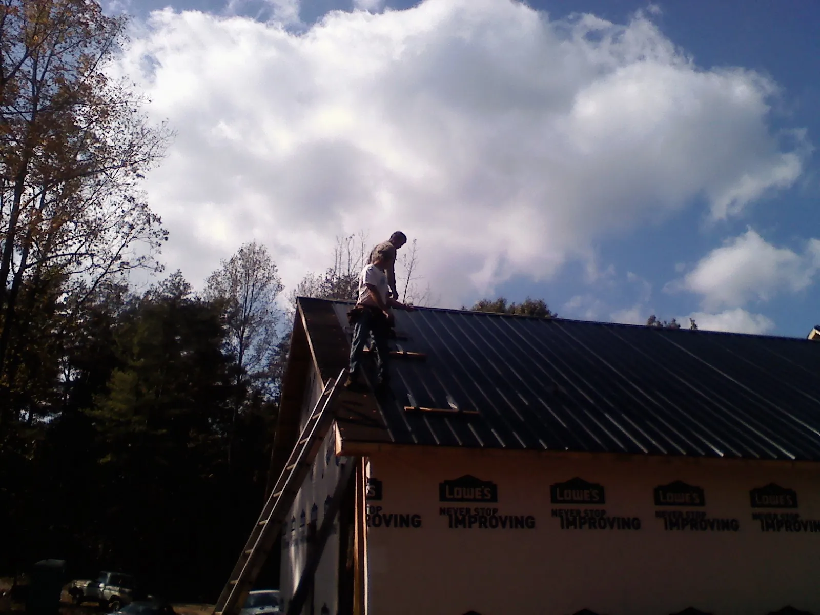 Roofer fastening dark metal panels high against a cloudy sky, from a Roof Inspection job in Cinebar