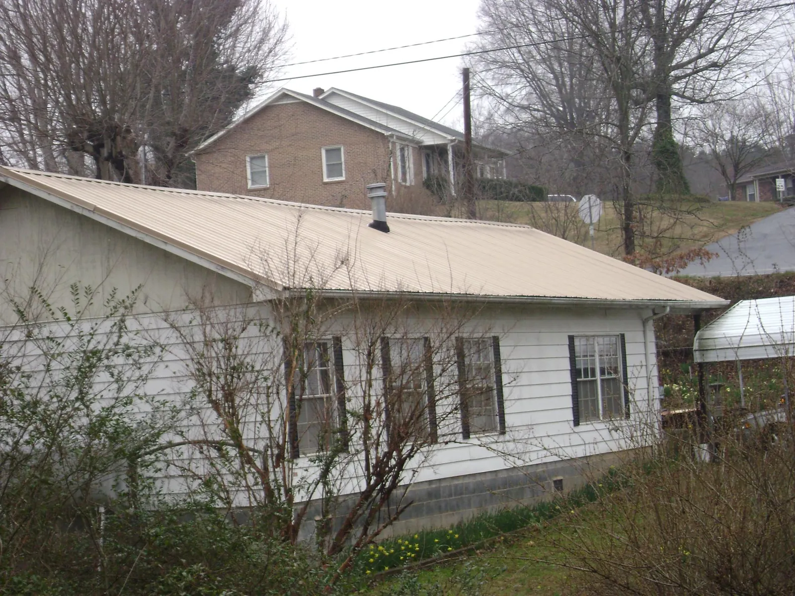 Tan metal roof on a white sided house set into a hillside — Commercial Roofing by Roofing Brothers in Cinebar