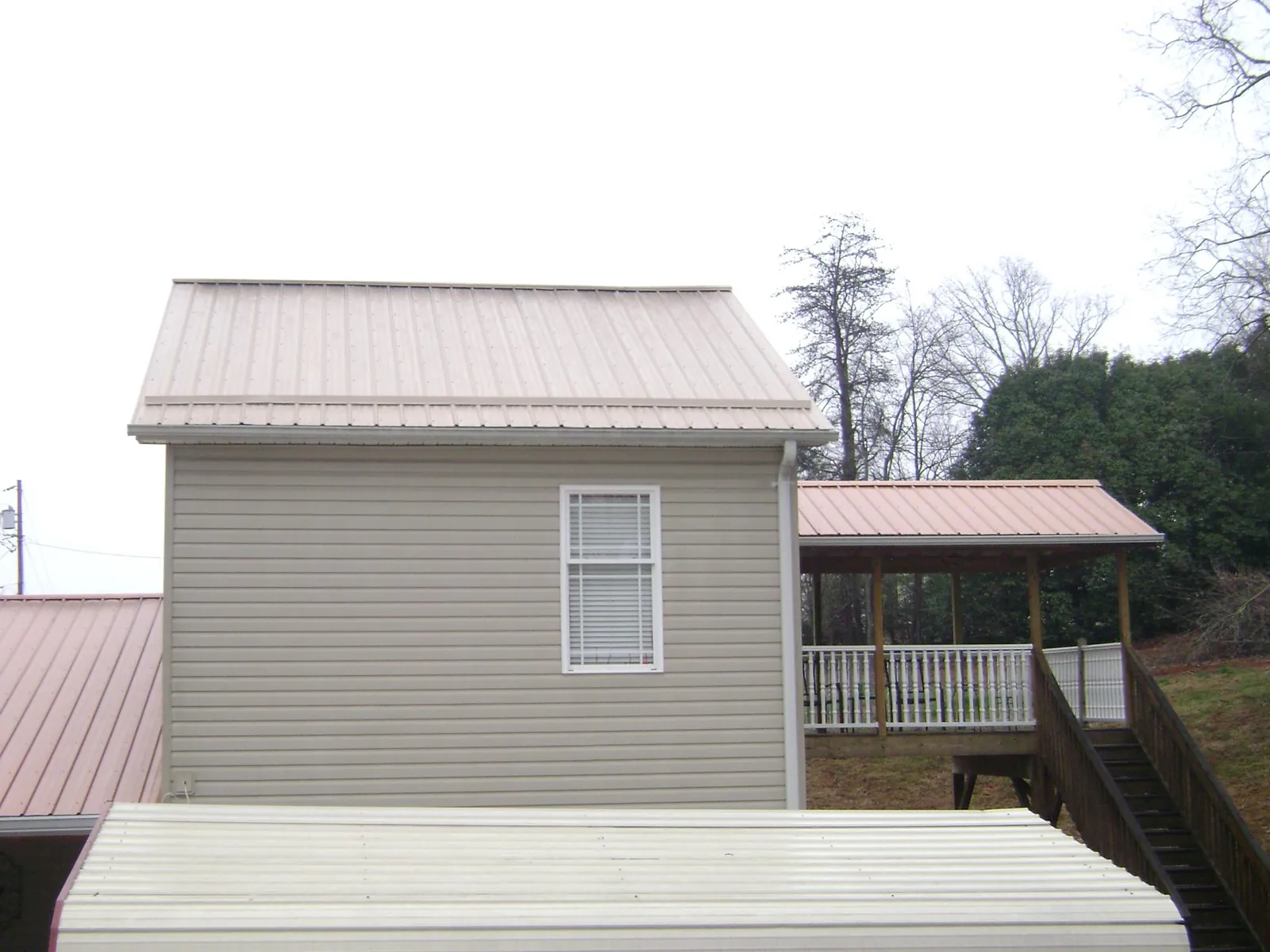 Tan metal roofs on a two story addition and attached porch, from a Roof Replacement job in Cinebar
